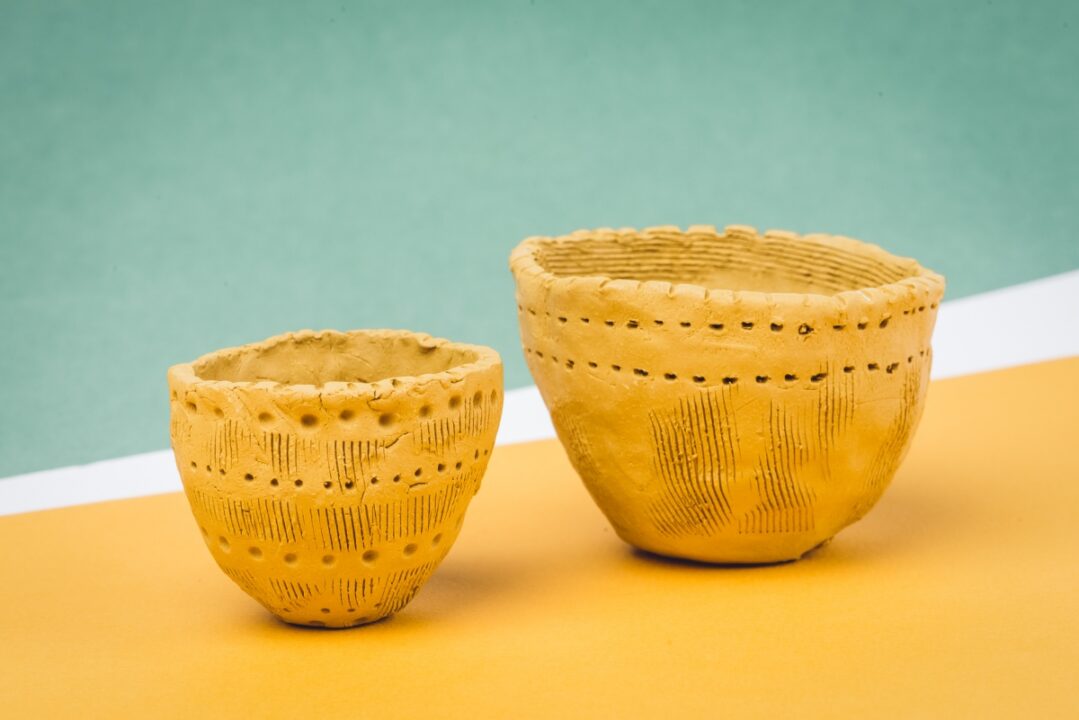 Kaks käsitööna tehtud savikaussi erineva suurusega, mille pinnal on jooned ja punktid dekoratiivsete motiividega.